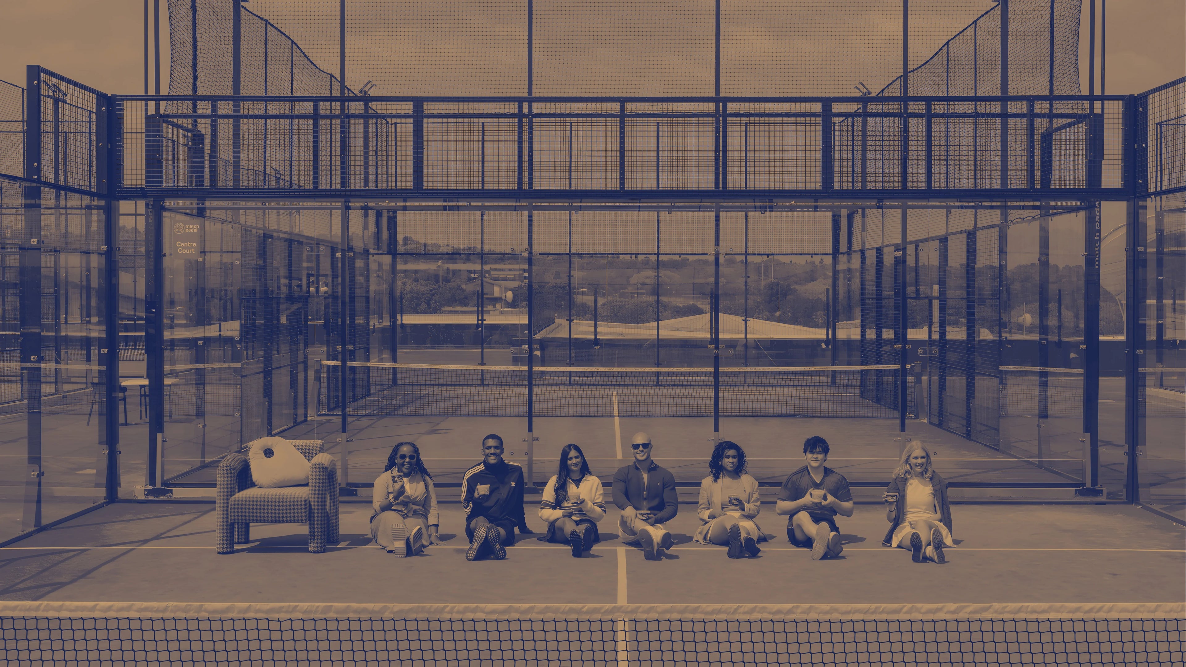 Group of people sitting on a padel court with a blurred effect, holding Hilo protein Puddings